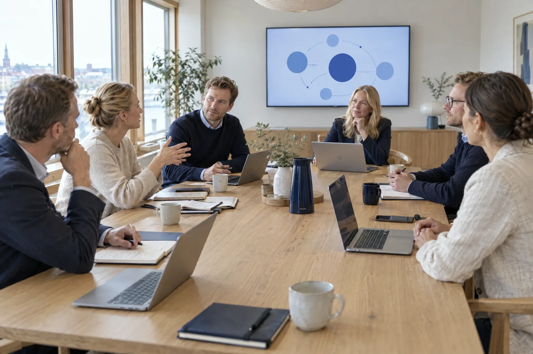 En ledergruppe diskuterer omkring et langt egetræsbord, mens en af dem stiller et spørgsmål